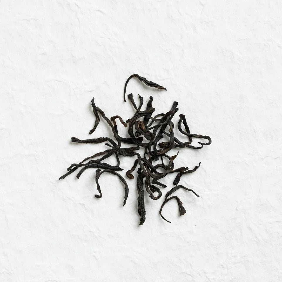 Fine dark twisted black-tea leaves on a pale textured surface.