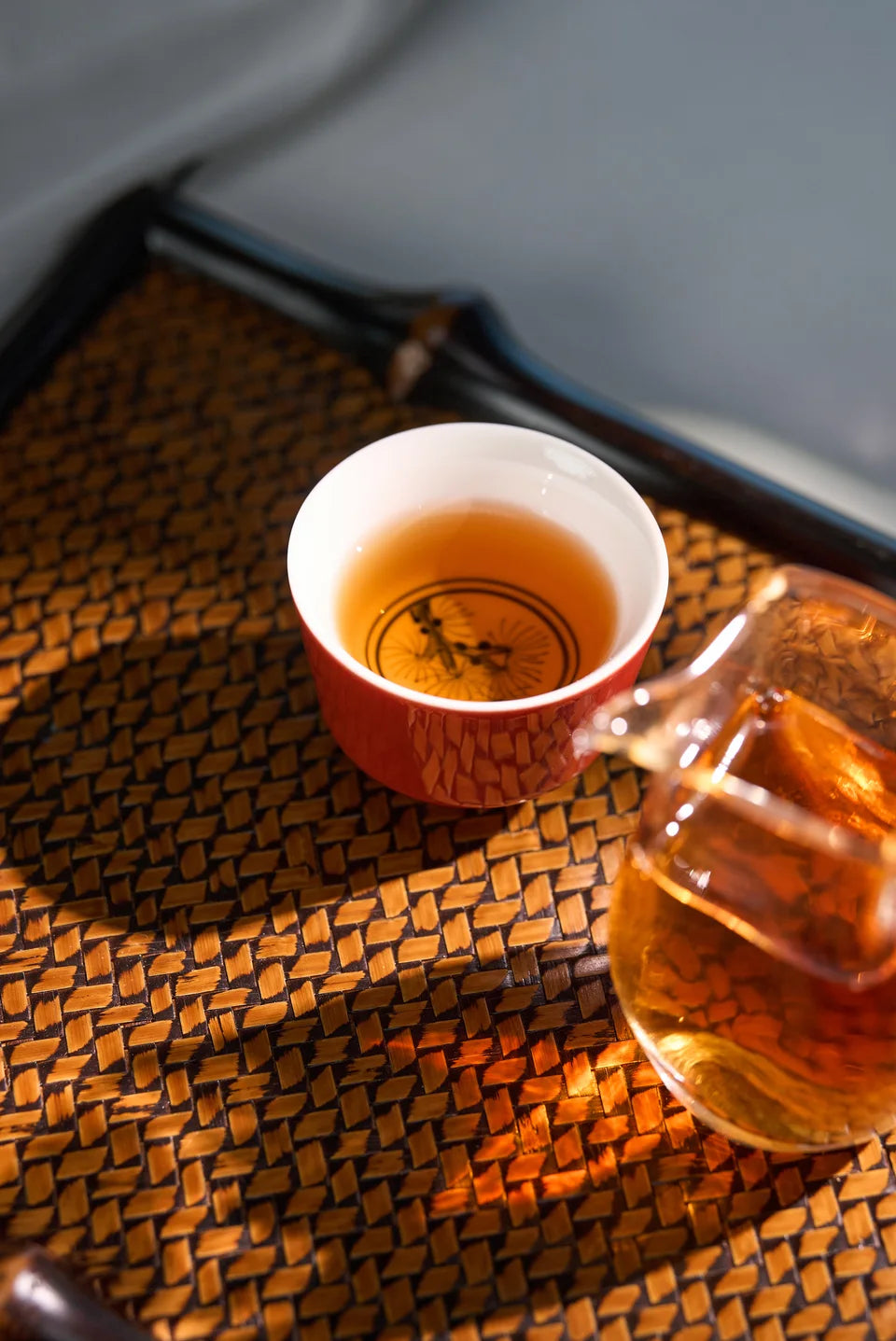 Amber black tea in a porcelain cup beside a glass pitcher on a woven tray.