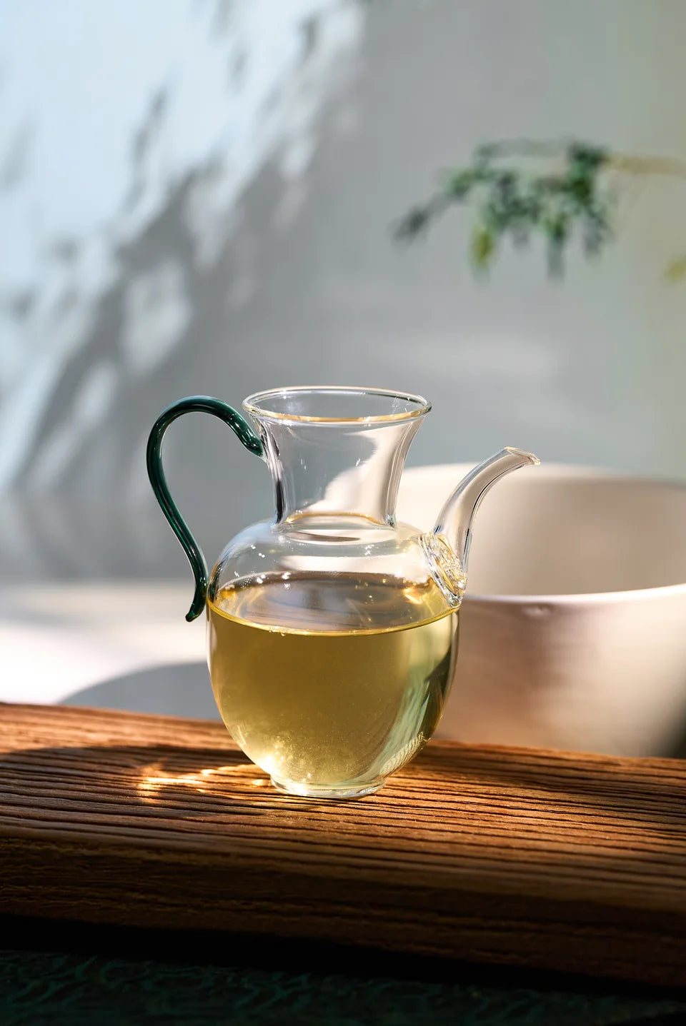 Pale green-gold tea in a glass pitcher with a green handle.