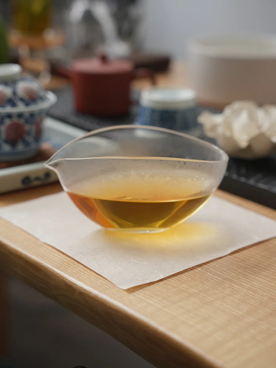A low glass pitcher with golden tea resting on a pale square coaster.