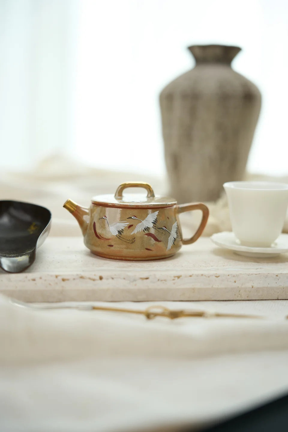 A decorated teapot and small white cup on a pale tea tray.