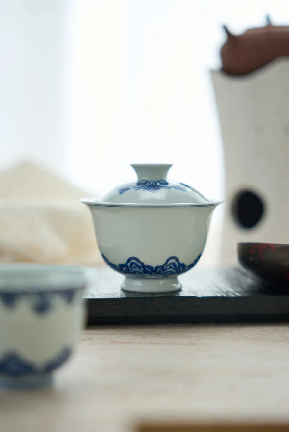 A blue-and-white gaiwan with its lid on a dark tea tray.