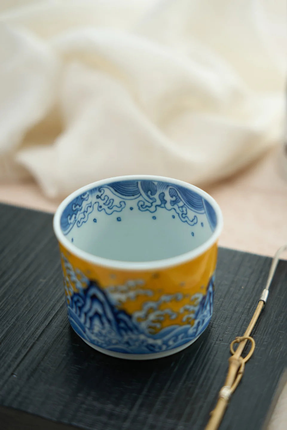 An empty yellow-and-blue porcelain cup on a dark tray.