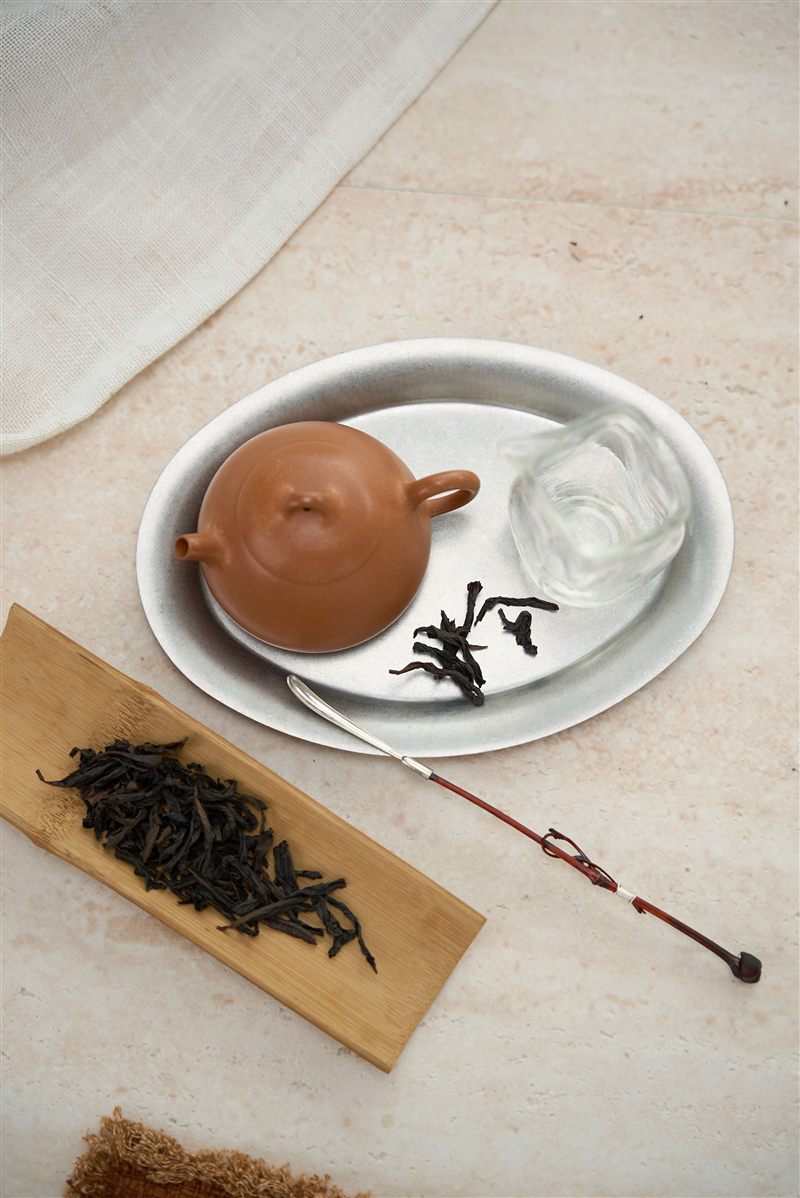 A small clay teapot, glass pitcher and tea leaves arranged on a tea tray
