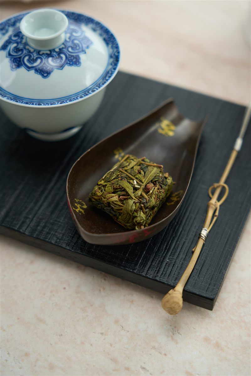 A blue-and-white gaiwan beside tea leaves in a wooden scoop