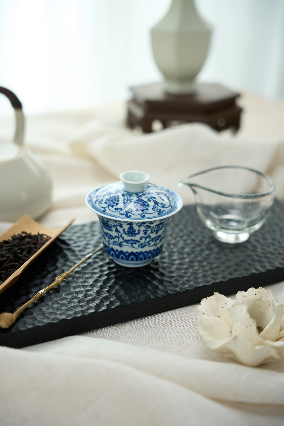 A blue-and-white gaiwan, glass serving pitcher and dry tea arranged for brewing
