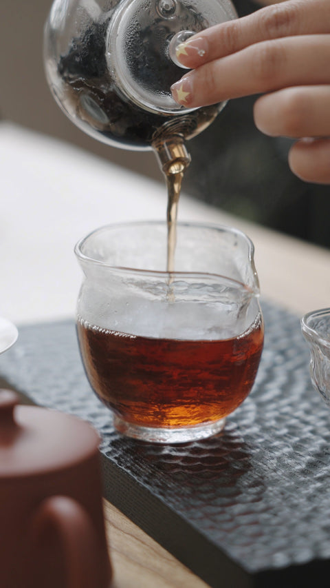 Amber tea being poured from a glass teapot into a serving pitcher.