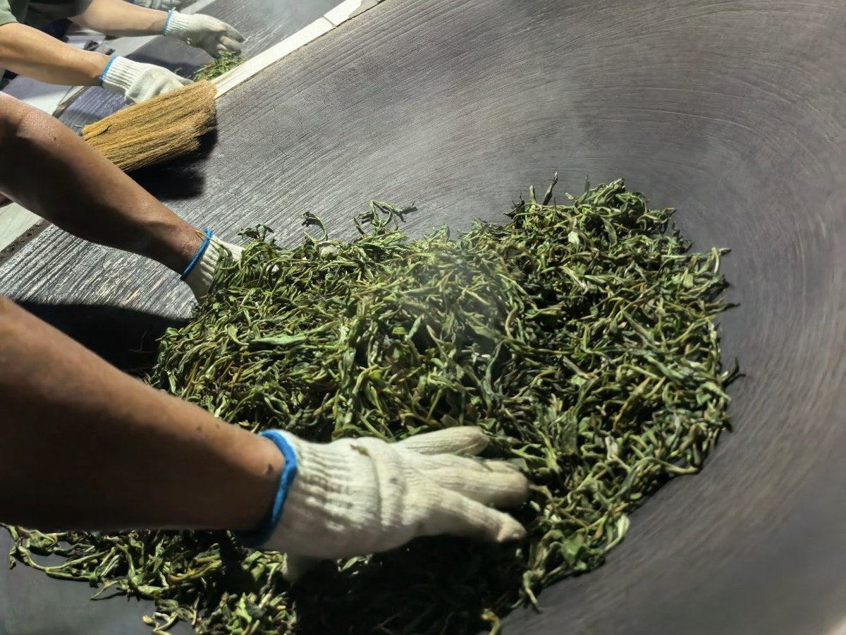 Hands moving tea leaves through a heated pan