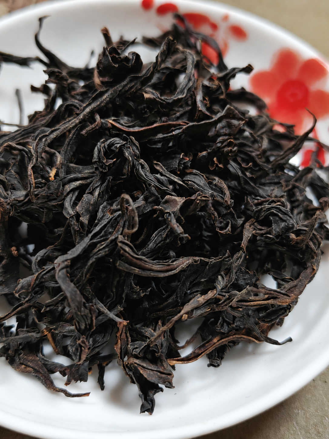 Dark twisted tea leaves on a patterned white plate