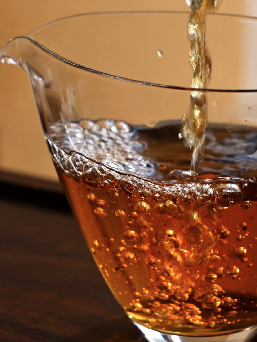 Amber tea being poured into a clear glass pitcher