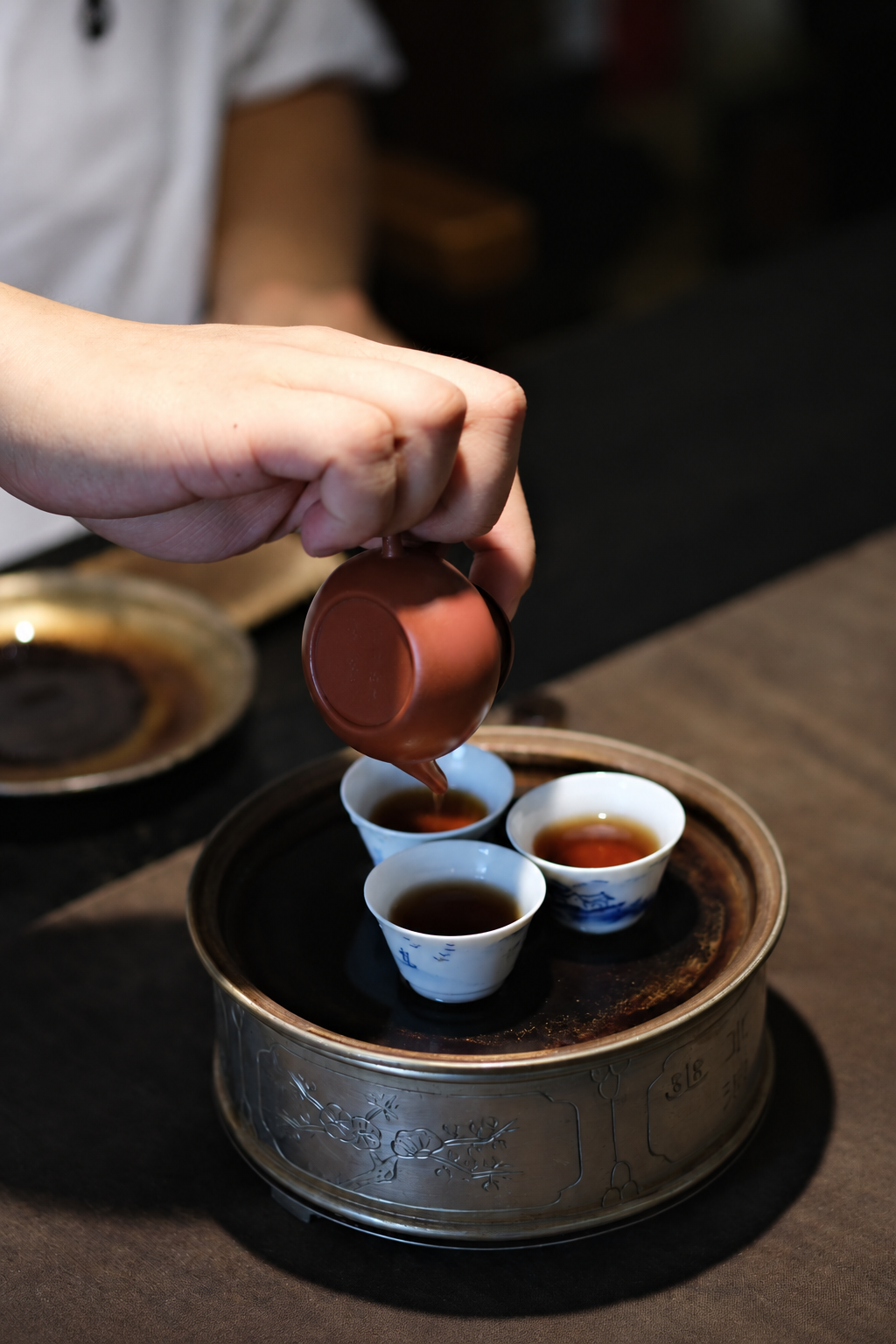 A hand pouring tea from a small clay pot into three cups