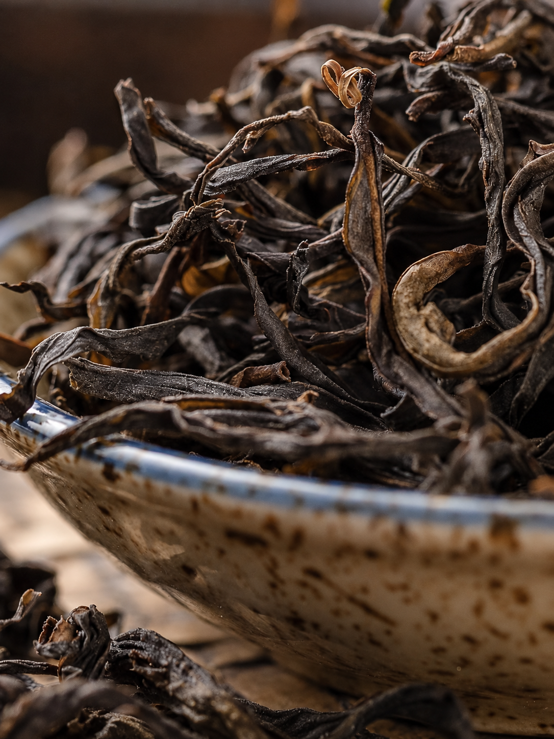 Long dark twisted tea leaves in a speckled bowl