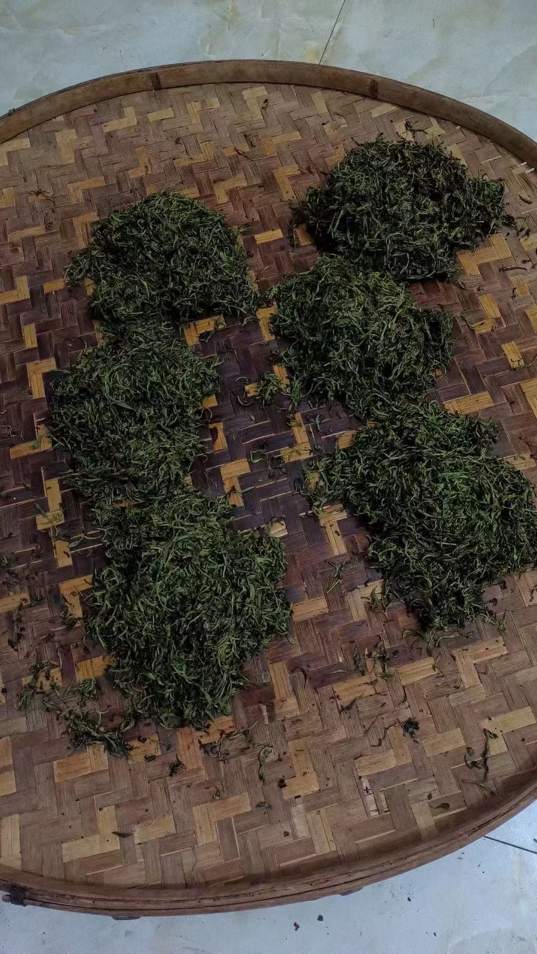 Small heaps of twisted tea leaves on a woven bamboo tray