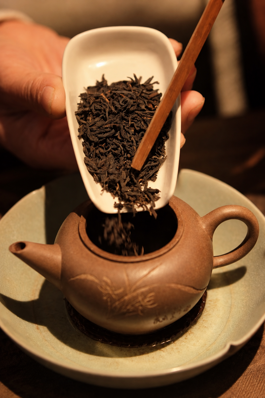 Tea leaves tipped from a white scoop into a clay teapot