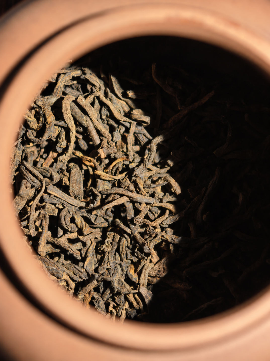 Dry tea leaves inside the mouth of a clay teapot