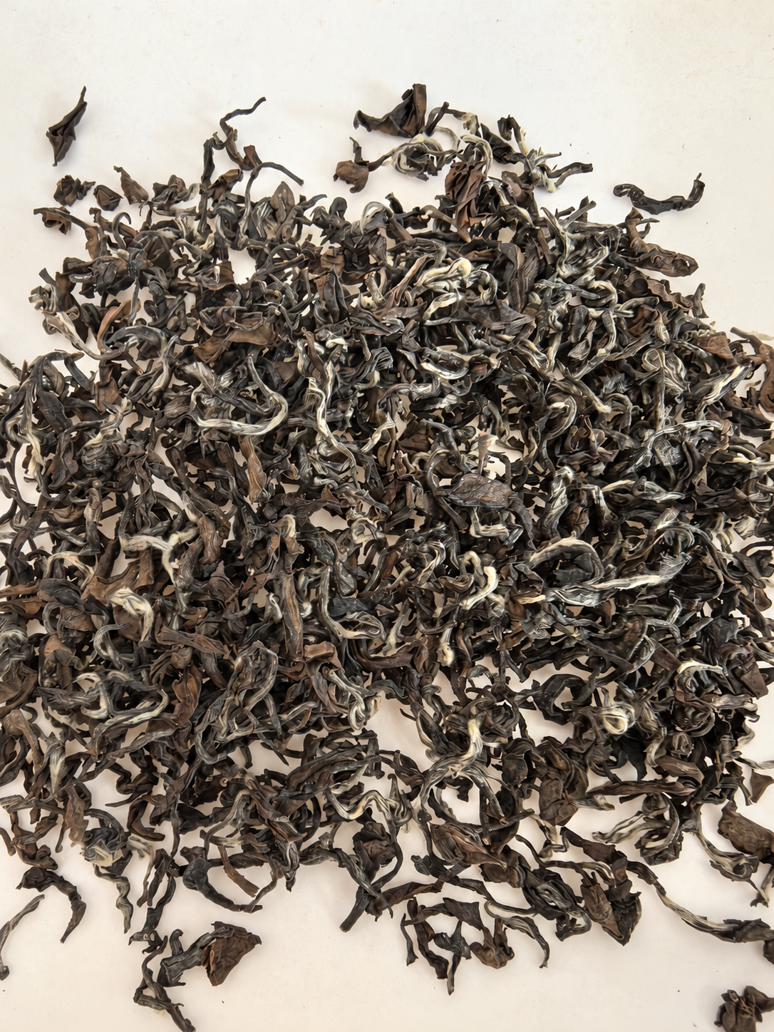 Curled dark tea leaves and pale buds on a light surface