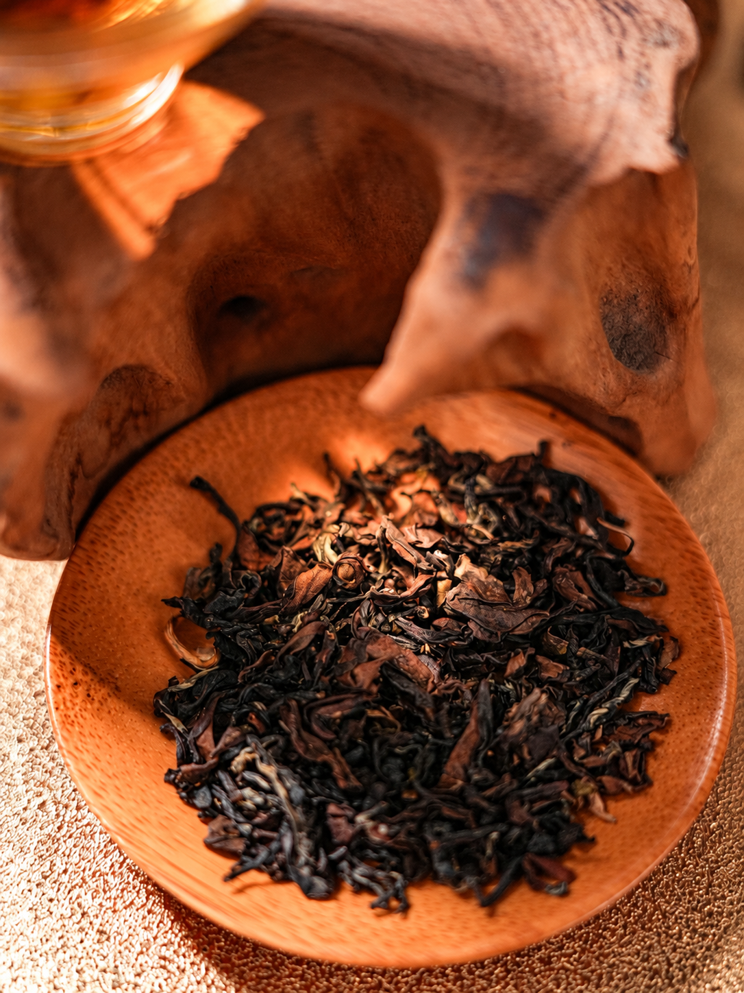 Curled dark tea leaves on a wooden dish in warm light