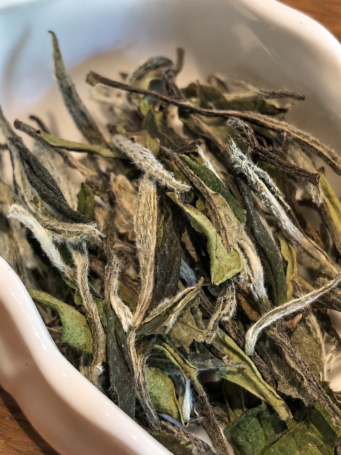 Down-covered tea buds and open dry leaves in a white bowl