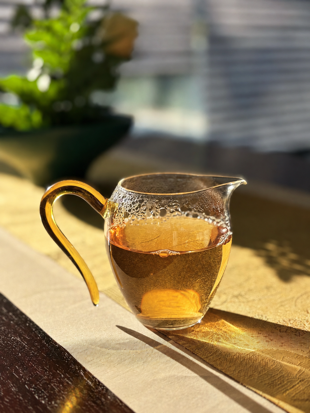 Golden tea in a clear glass pitcher with a handle in sunlight