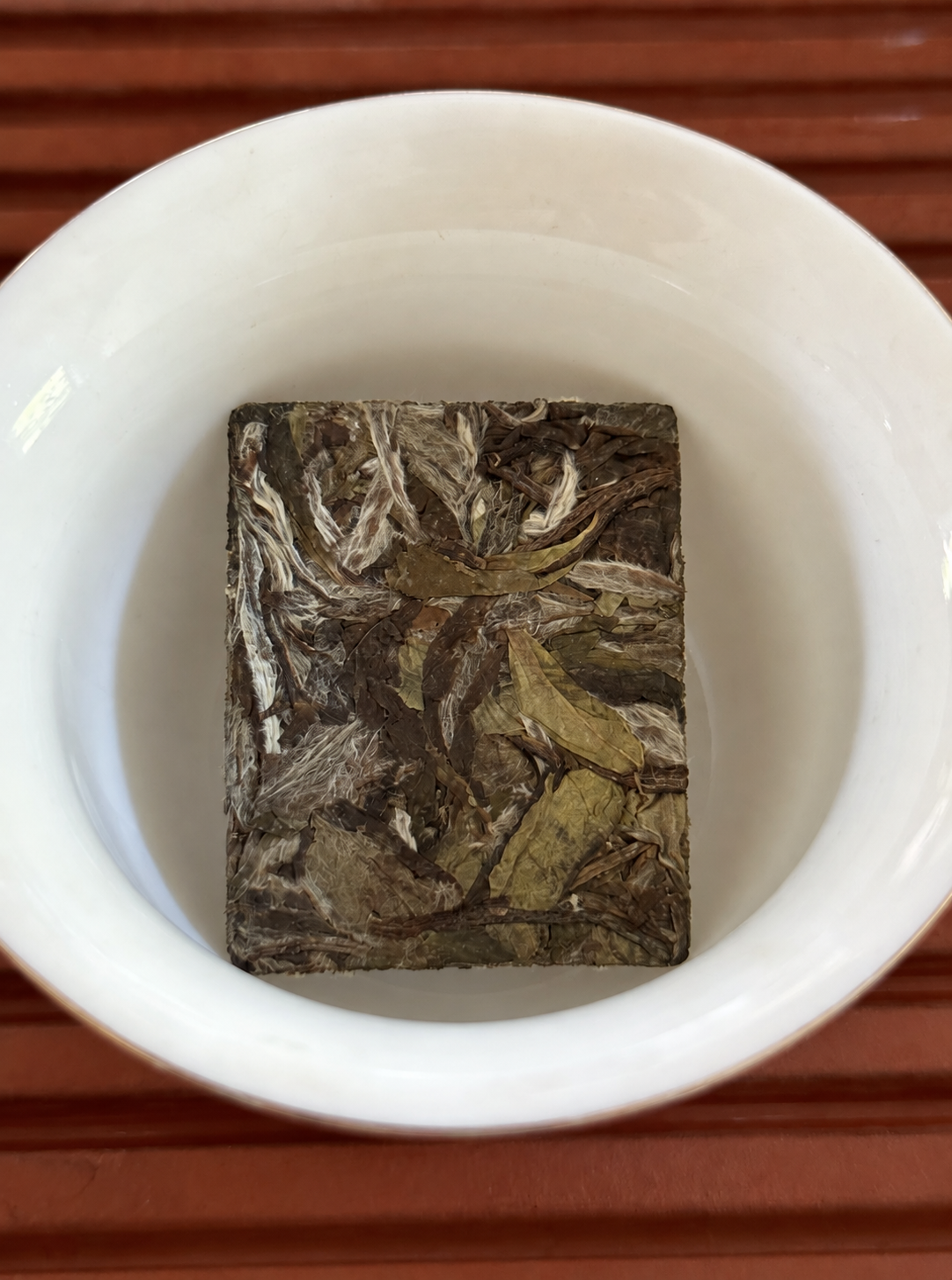 A rectangular pressed tea piece sitting inside a white brewing bowl