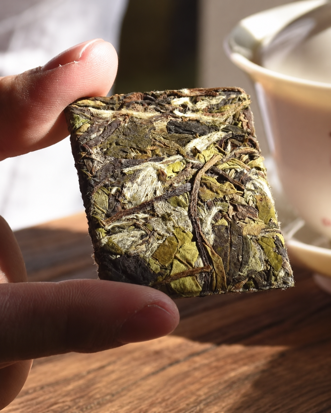 A small rectangular pressed tea piece held between fingers beside a white bowl