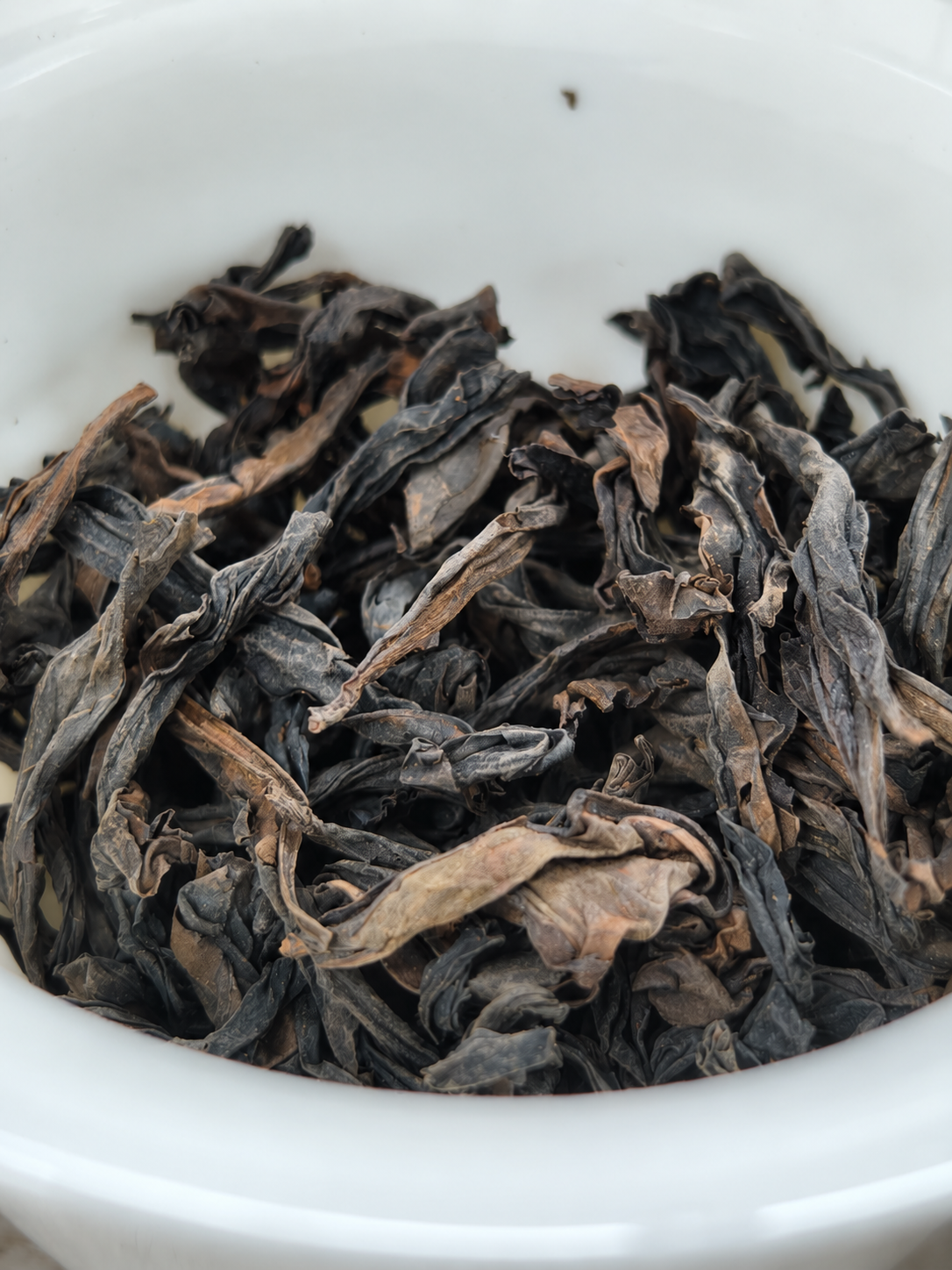 Dark twisted dry tea leaves in a white bowl