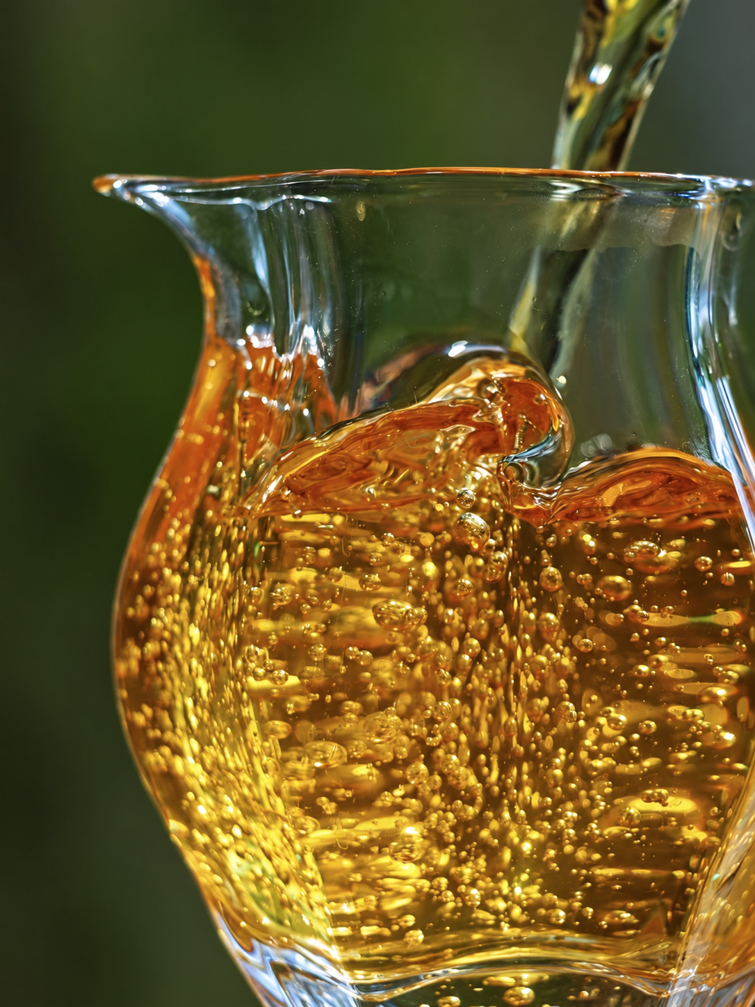 Golden tea flowing into a clear glass pitcher