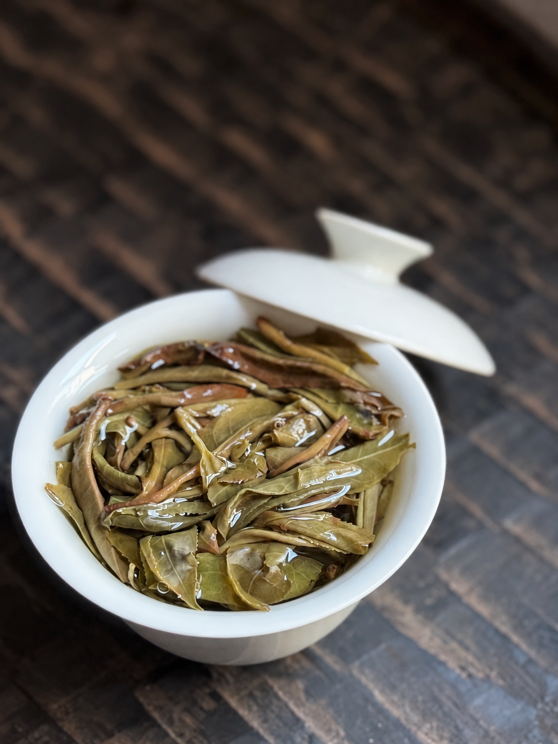 Opened leaves and stems in a white gaiwan with its lid beside it