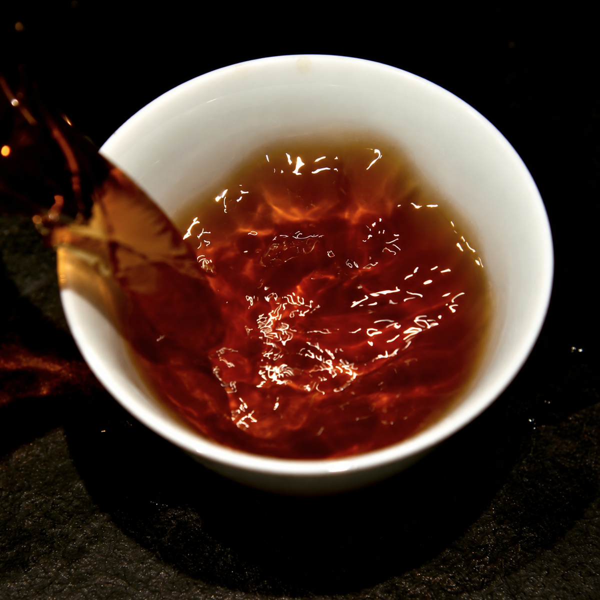 Reddish tea being poured into a white cup against a dark background