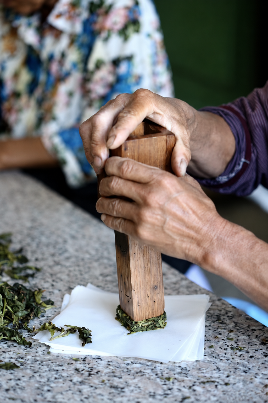 Hands lifting a wooden mold from a square of tea on paper