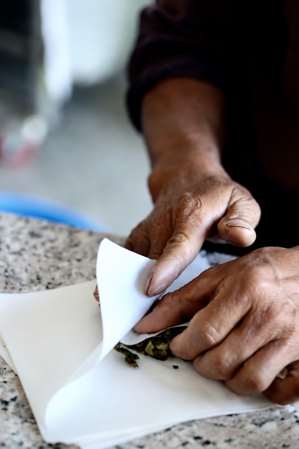 Hands folding white paper around a square of tea