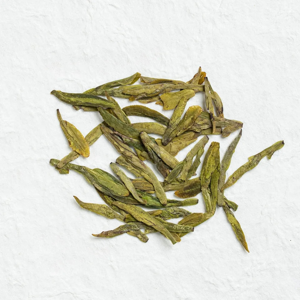 Flat green Longjing leaves on a pale textured surface.